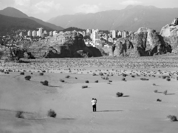Don't wait up! Man in desert with small child in his arms on mobile phone, by Denis Taylor