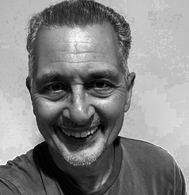 Smiling man with short grey hair and a light beard, wearing a t-shirt.